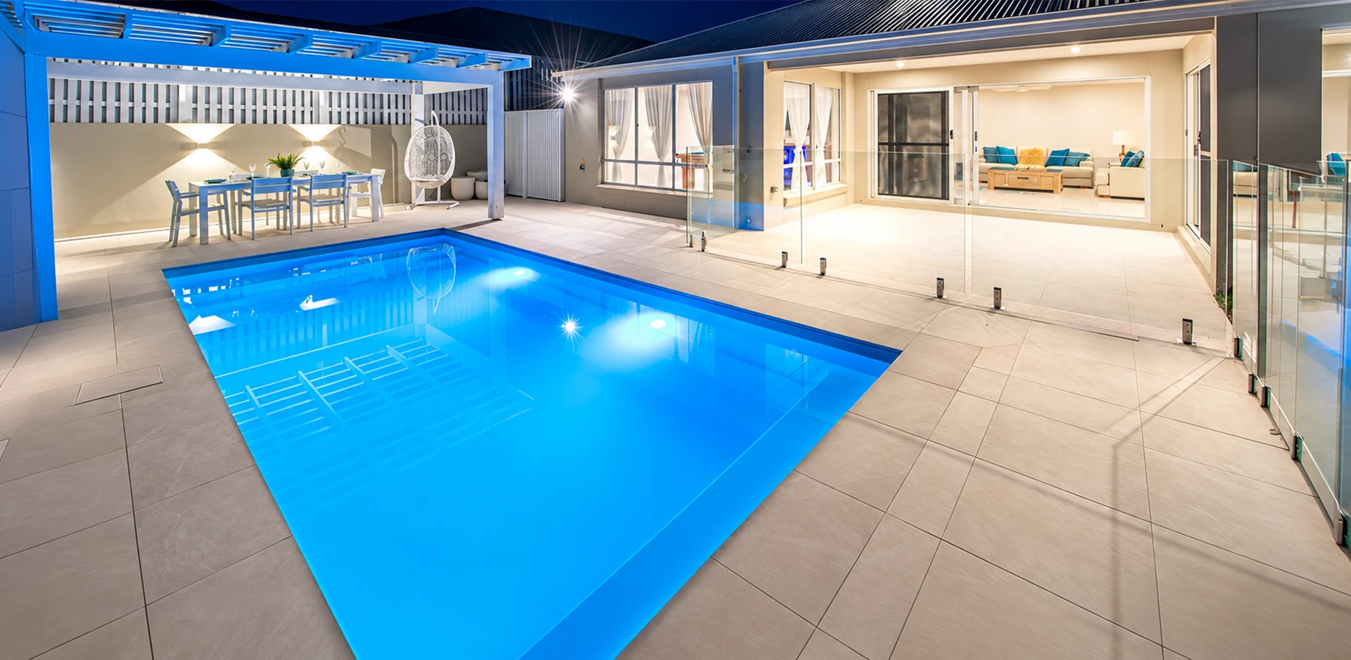 A 7m Entertainer pool lit at night beside an Aquatime Pools home